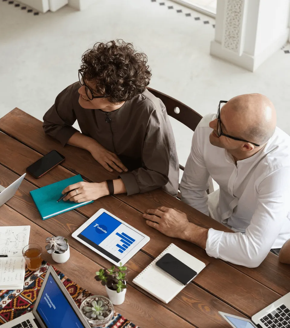 Conseil en réunion d’affaires Gestion des publicités Deux professionnels en réunion discutant autour d'une table avec tablettes et documents.